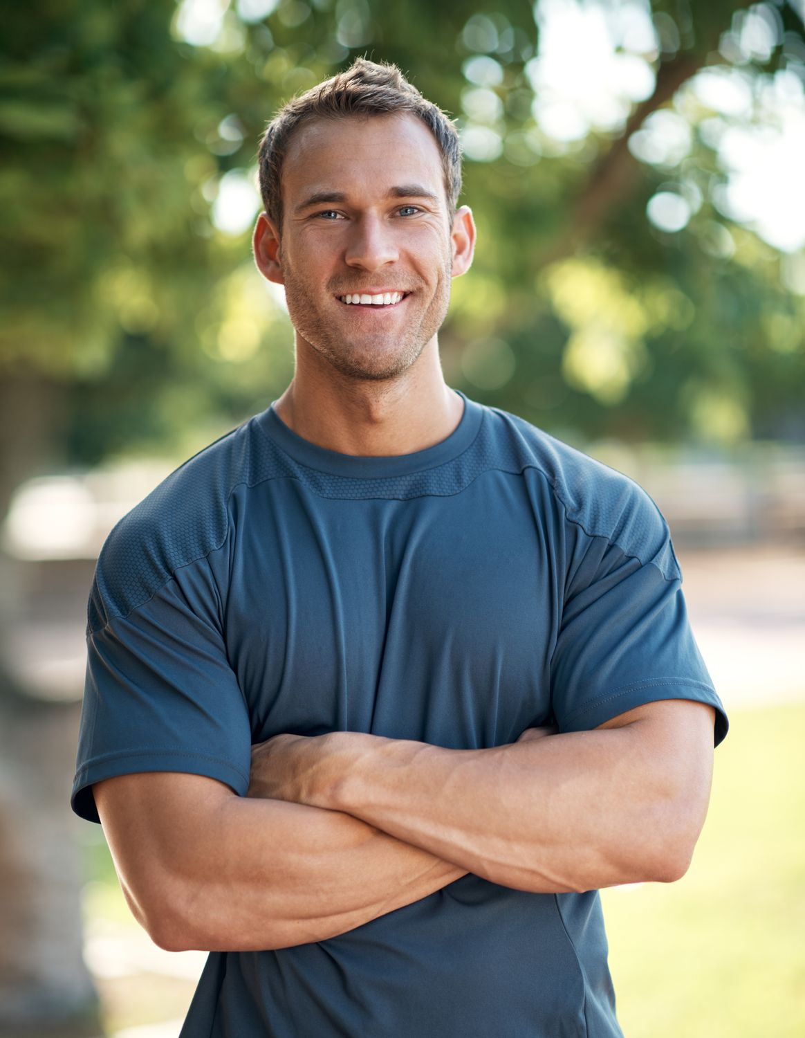 Smiling man with crossed arms outdoors.