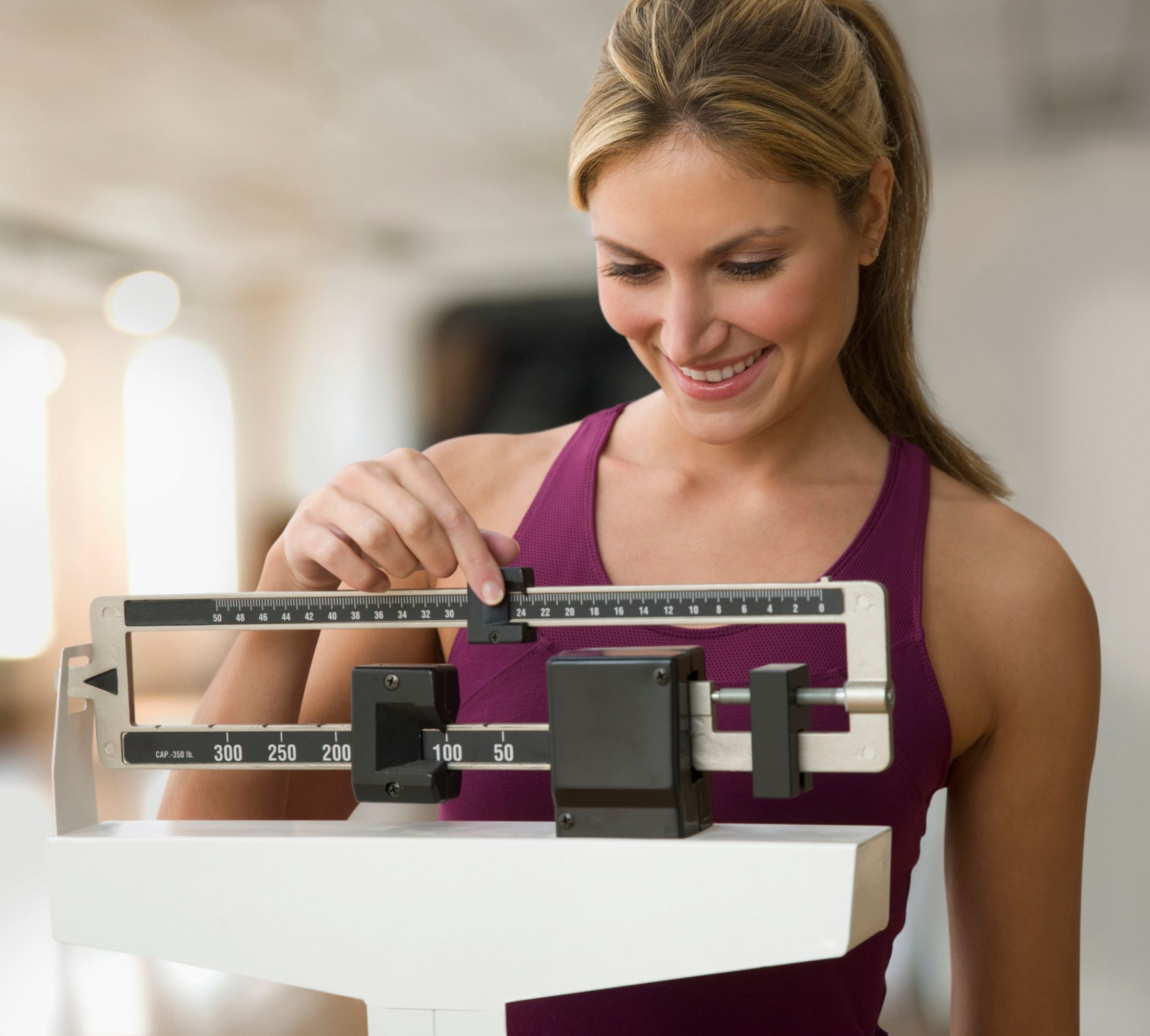 Woman adjusting weights on a scale in gym.