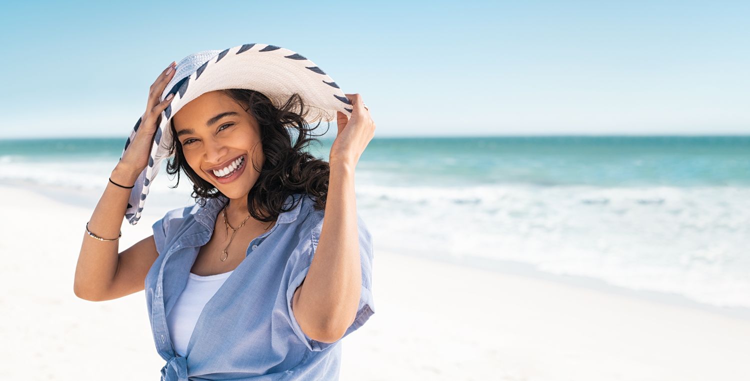 Smiling woman in hat at the beach.