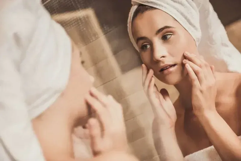 young woman examining skin in mirror thinking about laser skin resurfacing treatment